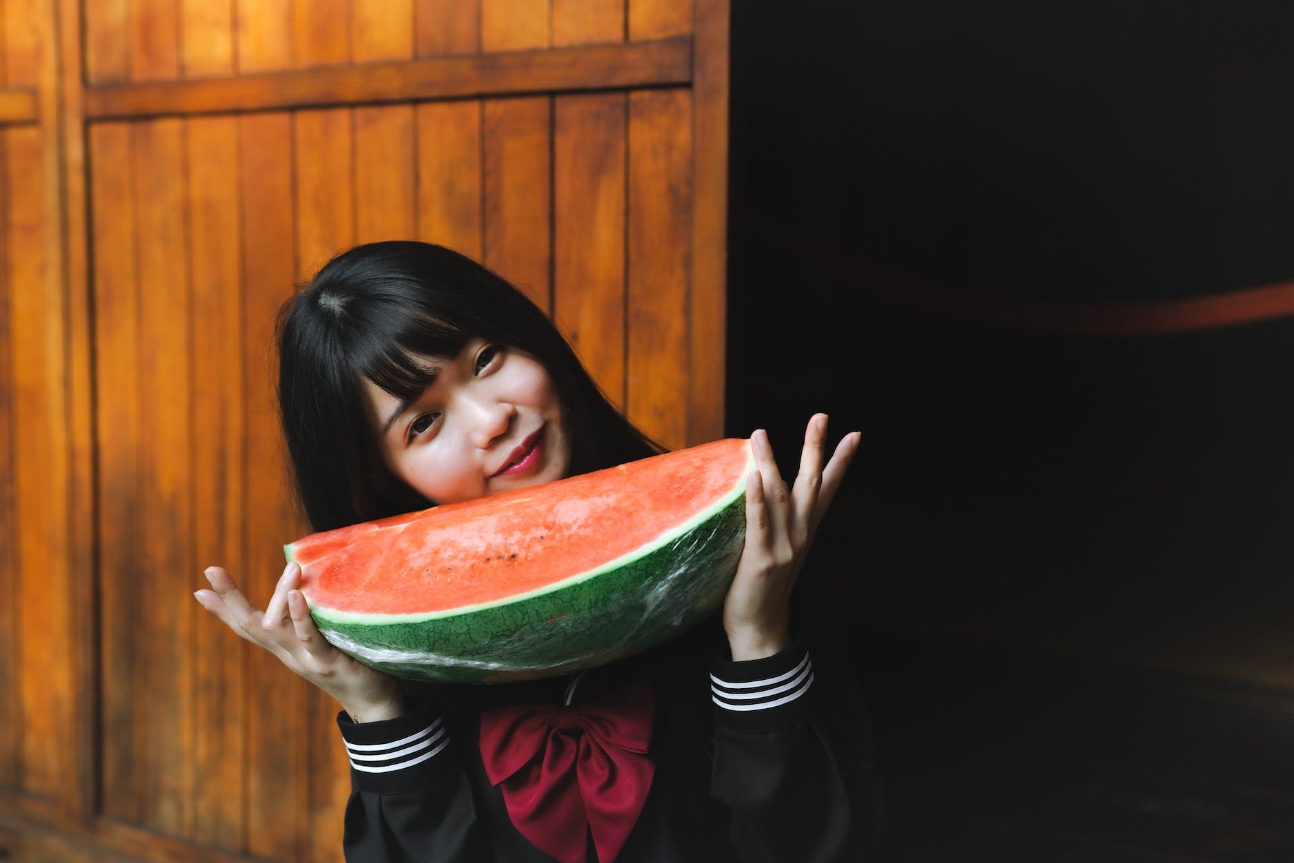young girl in a japanese school uniform holding a watermelon
